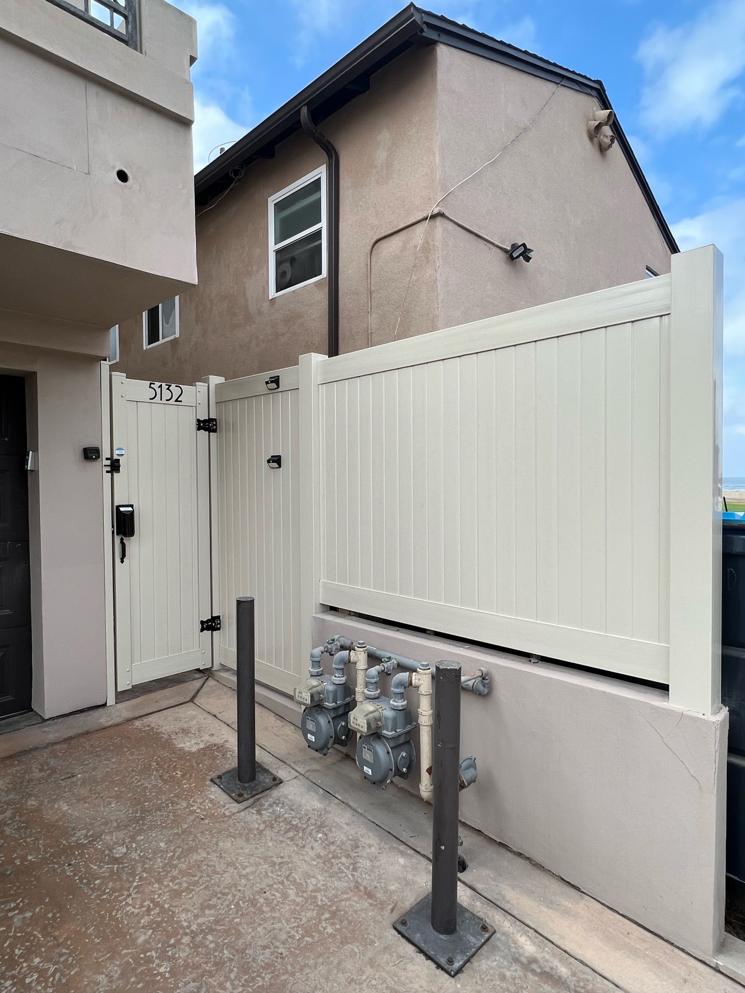 Beige fence with a gate protecting gas meters; adjacent building in the background.