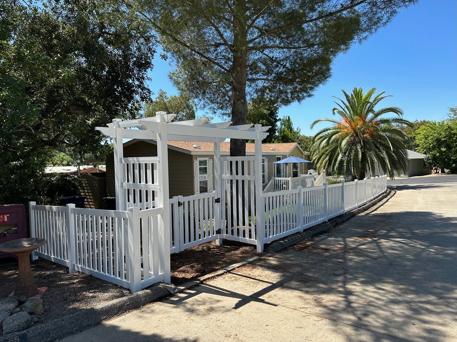 White picket fence and pergola in front of a house, sunny day.