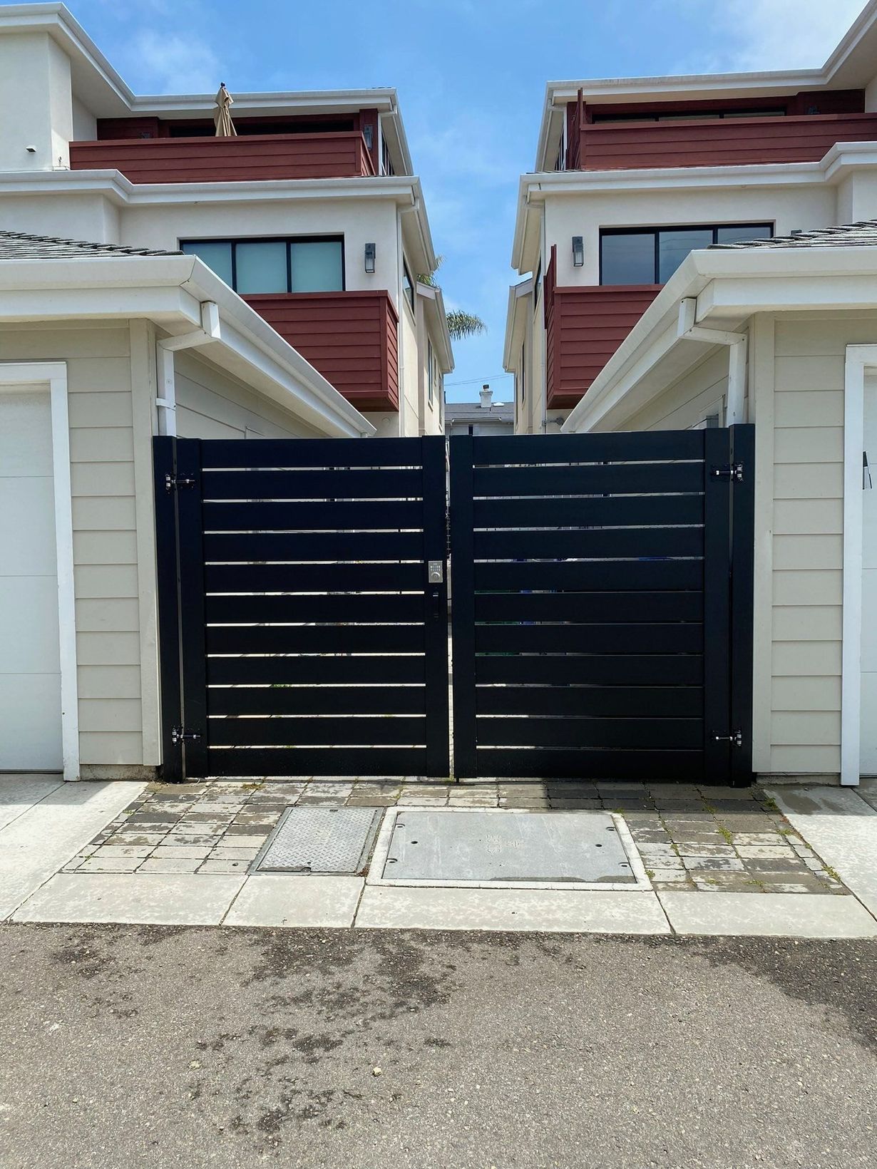 Black gate between two beige buildings with red roofs. Paved area in front.