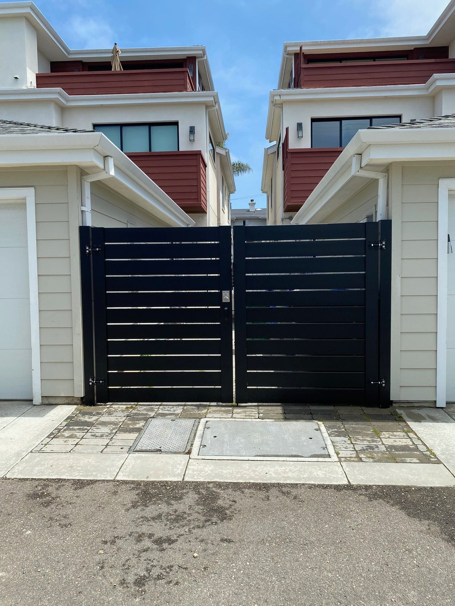 Black gate between two beige buildings with red roofs. Paved area in front.