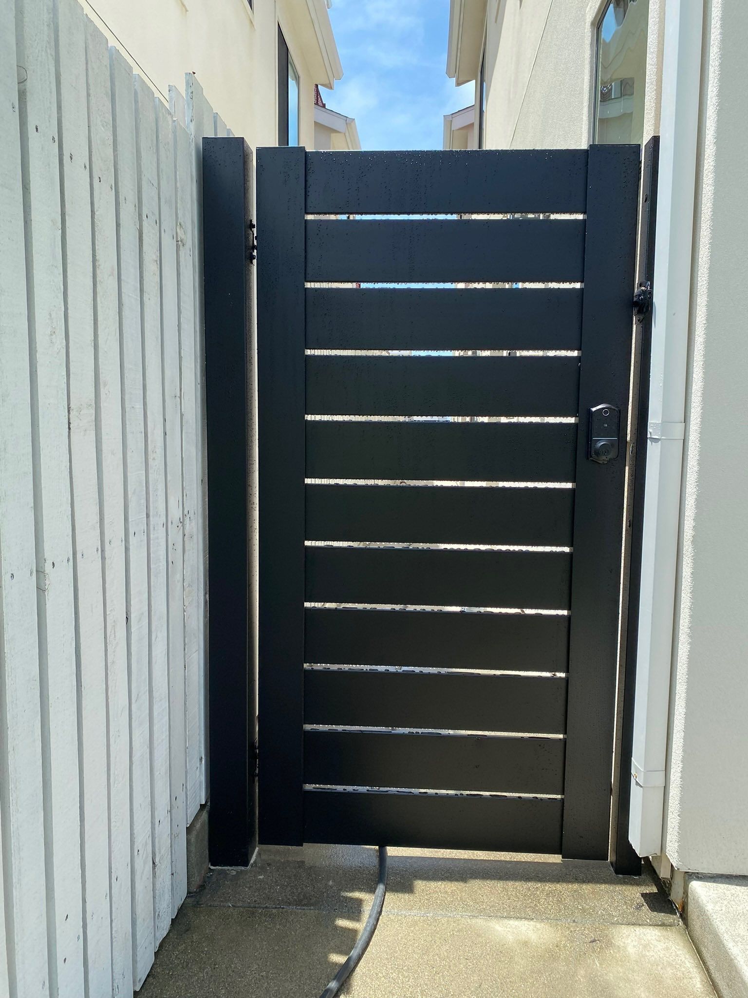 Black horizontal slat gate between white concrete walls on a sunny day.