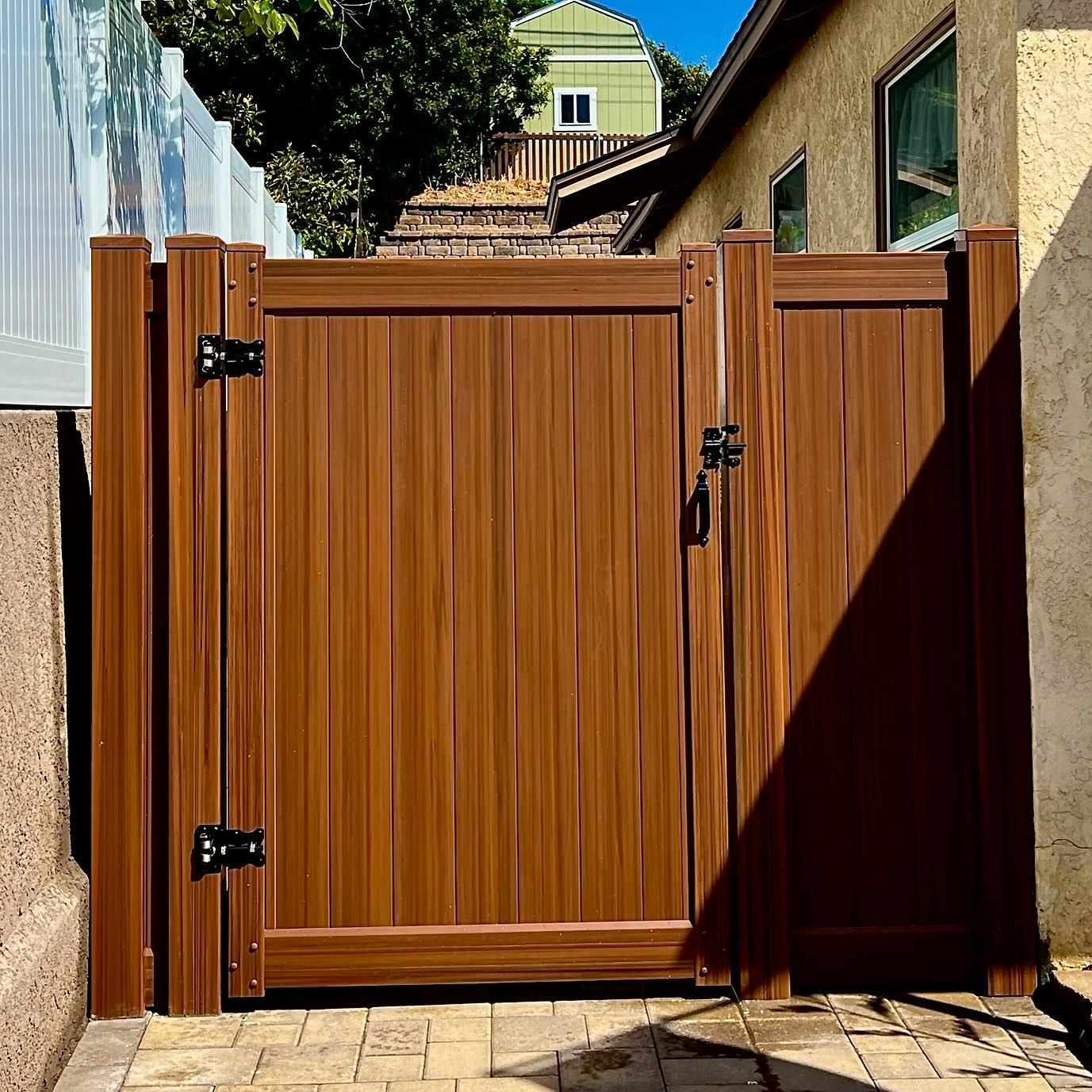 Brown wooden gate in a residential setting, secured with black hardware.