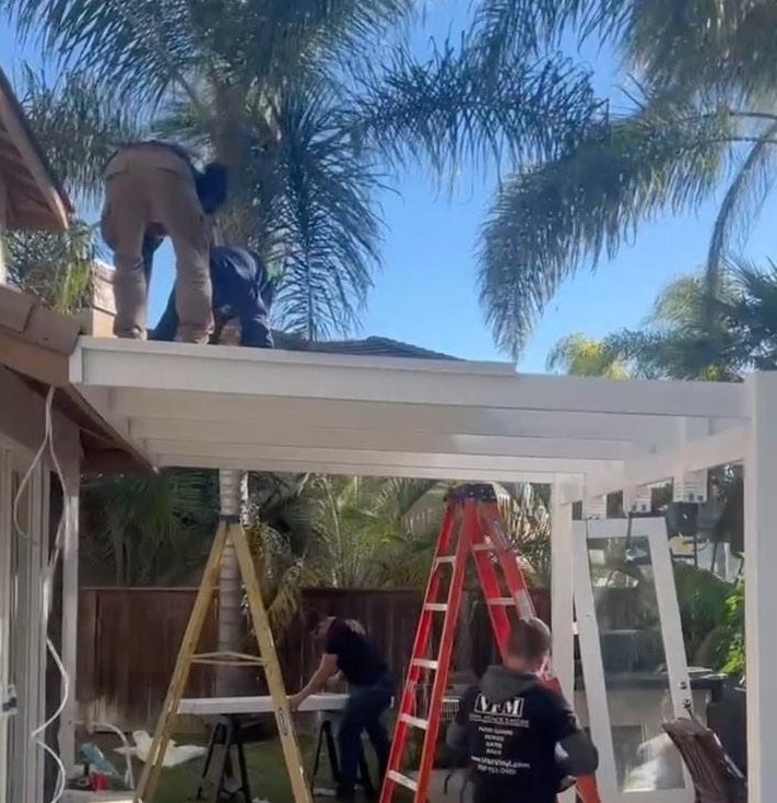 Workers constructing a white patio cover on a sunny day, using ladders and tools.