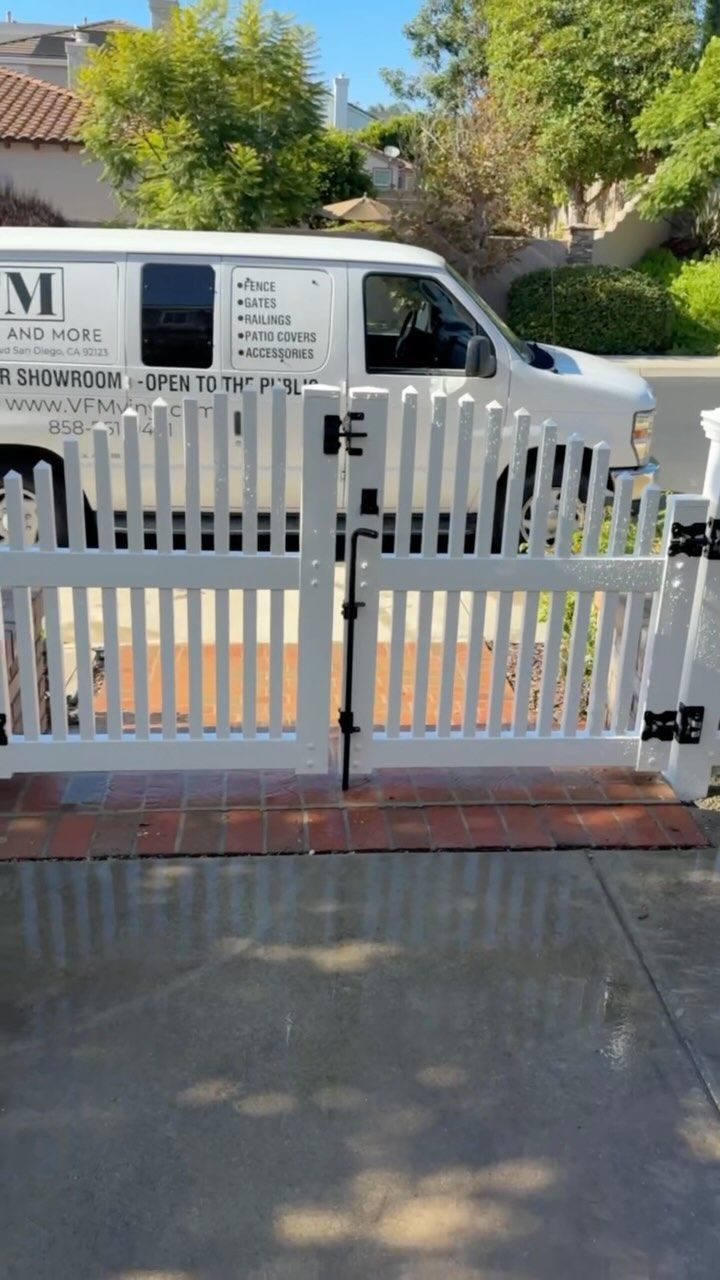 White picket fence gate open on a brick base, with a white van in the background.