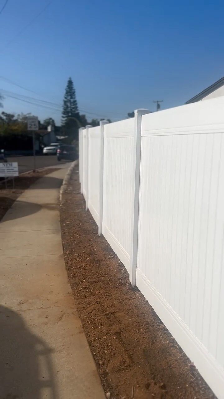 White vinyl fence along a sidewalk with a gravel bed, under a blue sky.