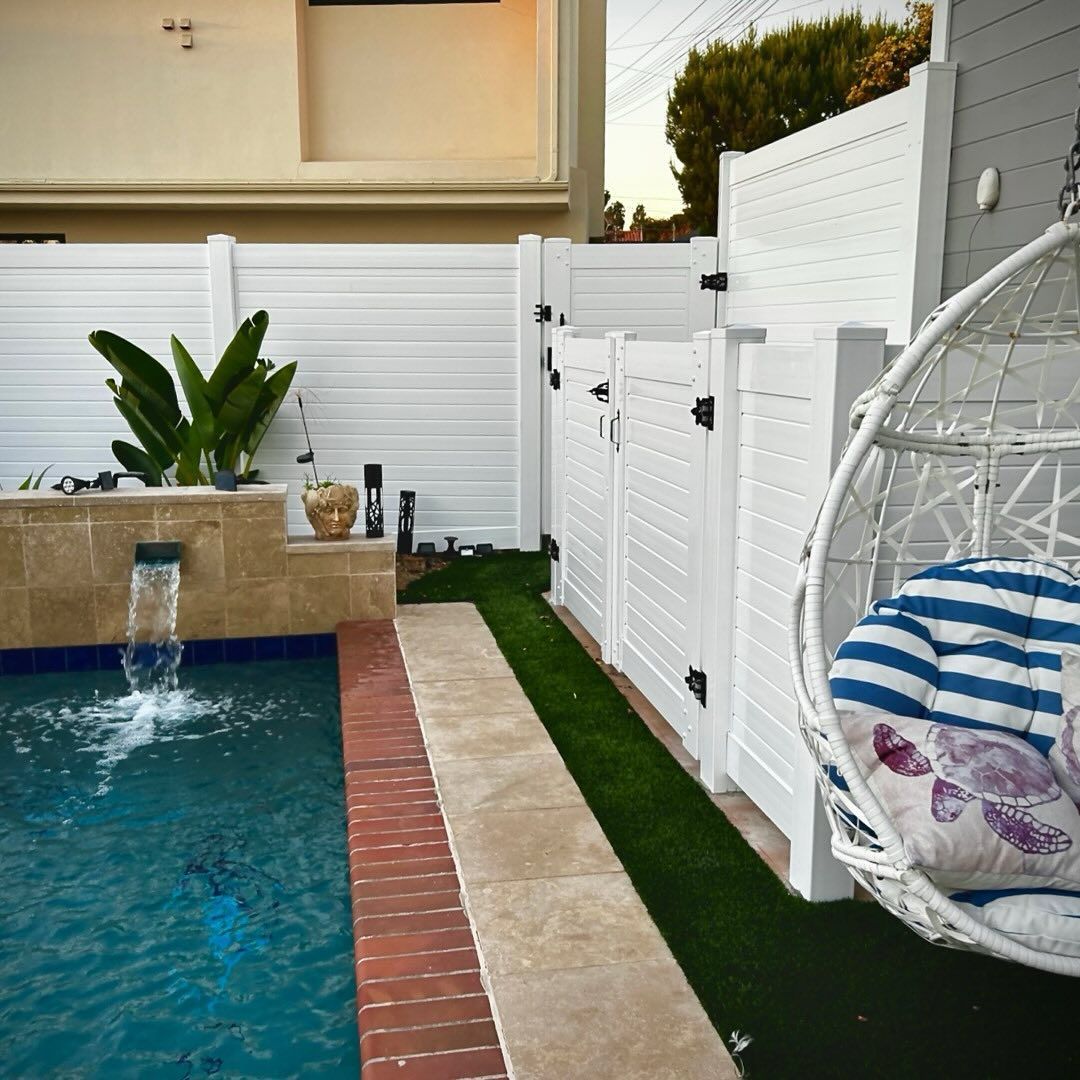 Backyard with pool, white fence, hanging chair, and artificial grass.