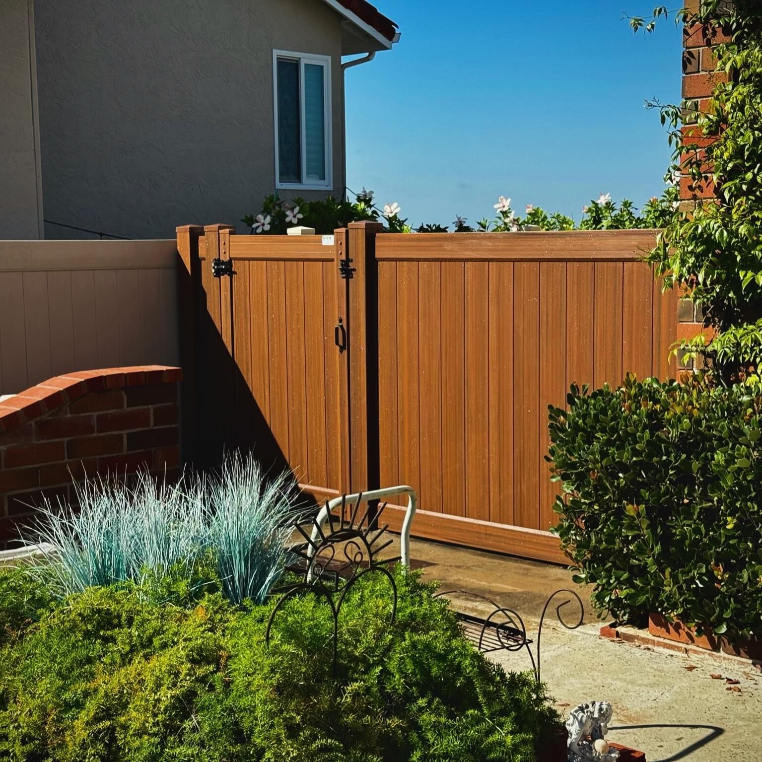 Brown wooden gate in a garden, partly open, surrounded by plants and a brick wall.