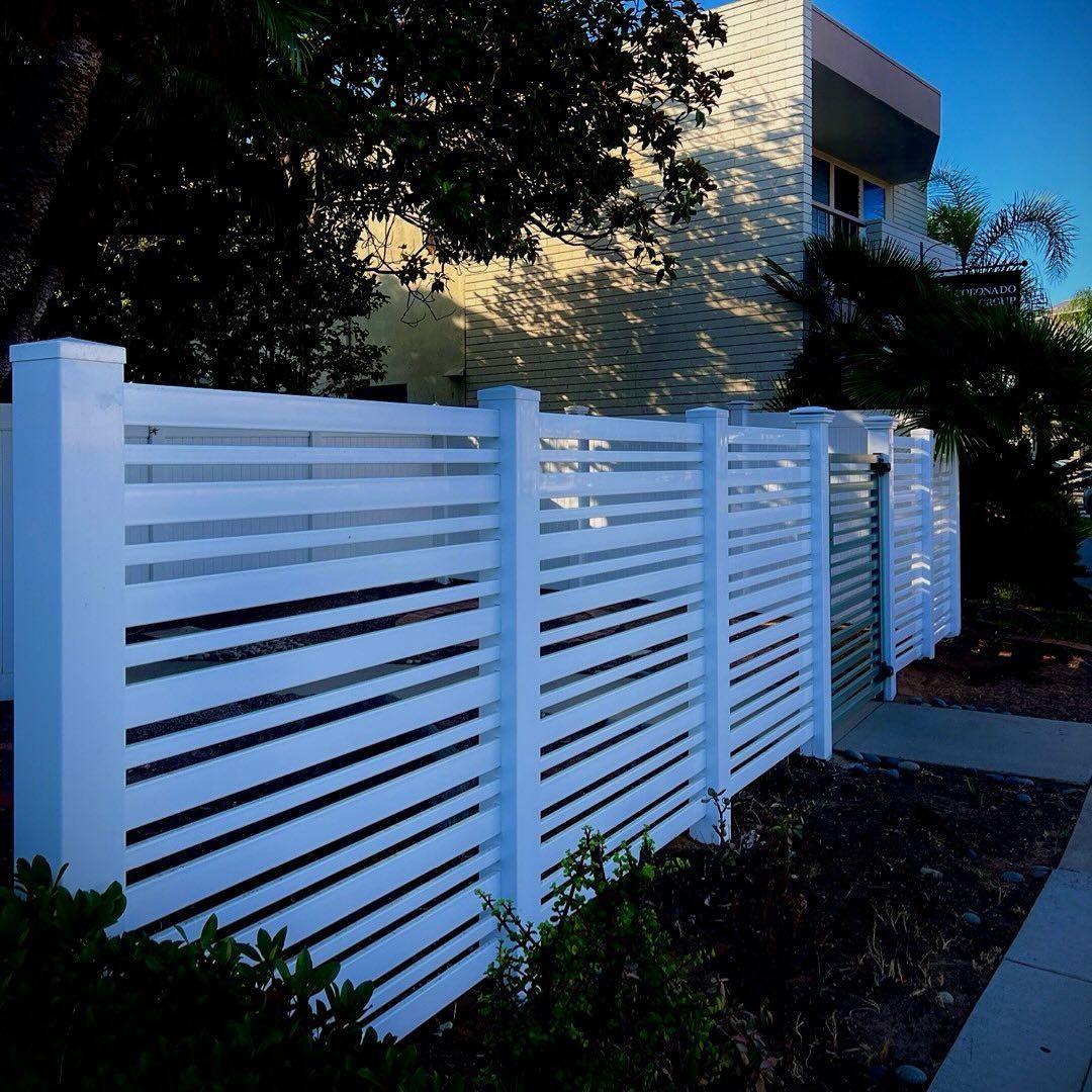 White horizontal slat fence in front of a building and foliage.
