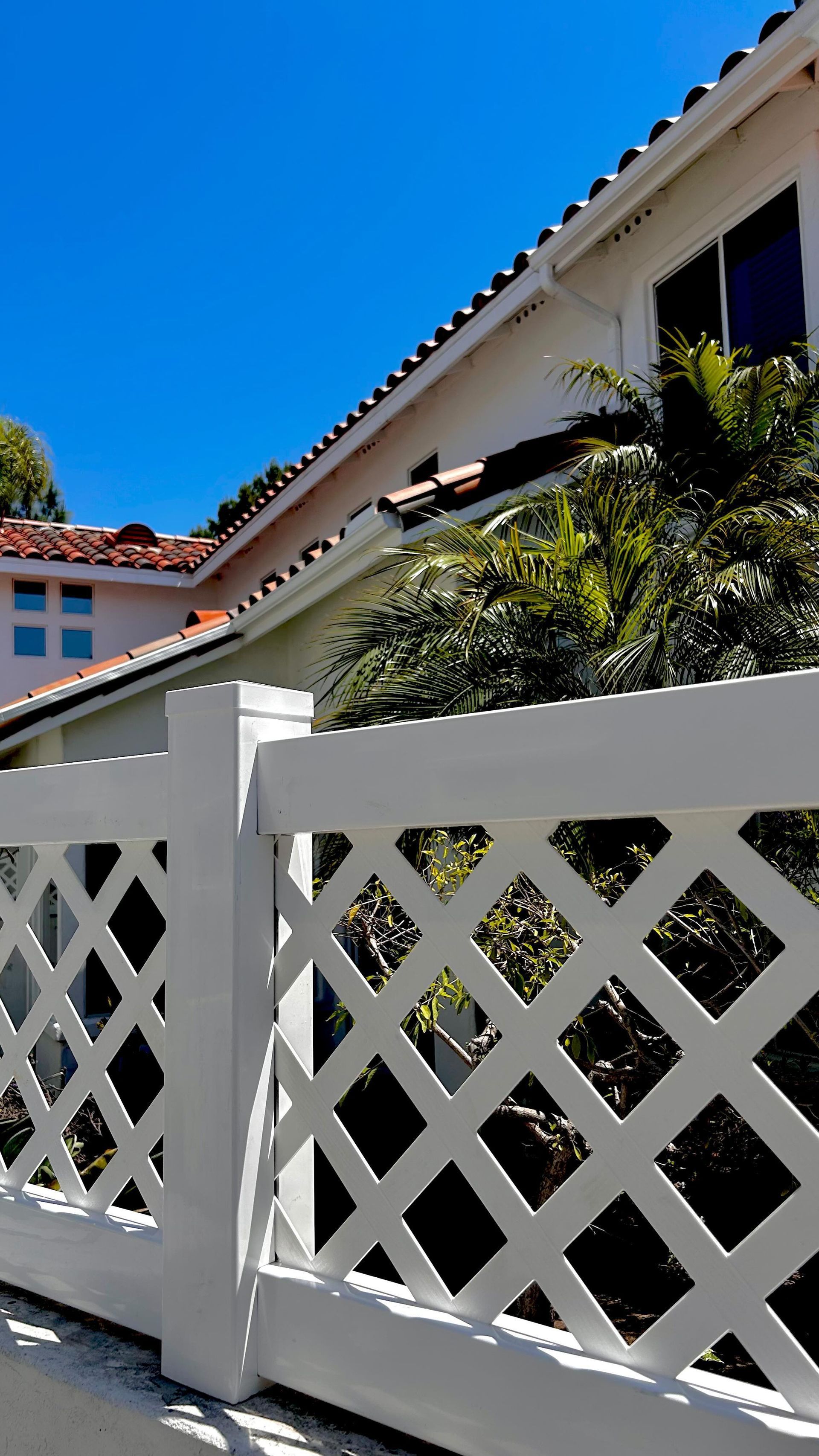 White lattice fence in front of a two-story house with red tile roof and blue sky.