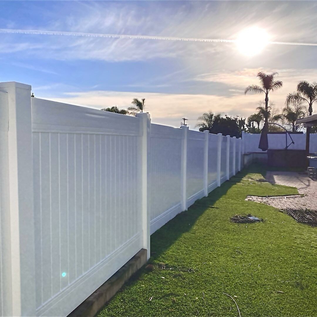 White vinyl fence along green lawn under a sunny blue sky.