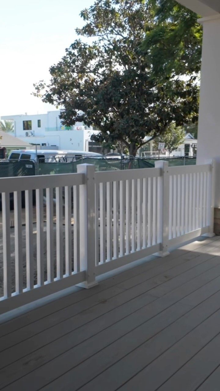 White picket fence on a wooden deck with a large tree in the background.