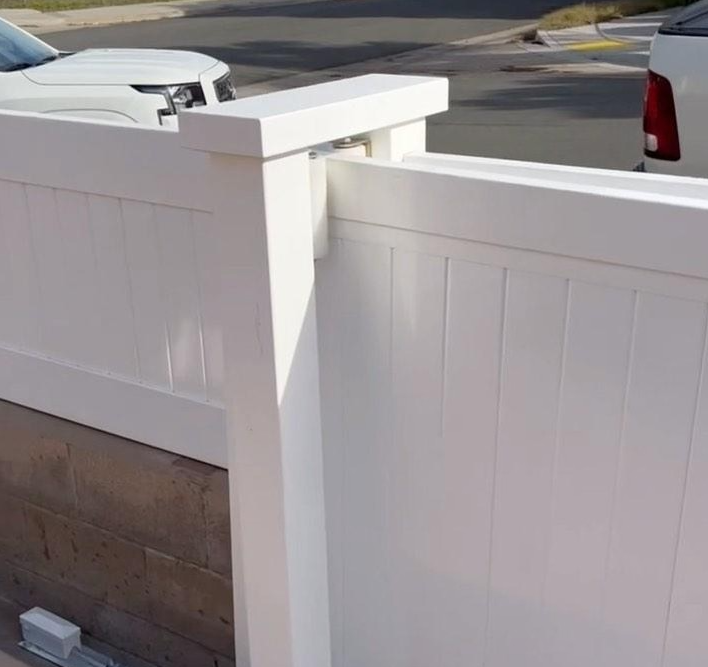 White vinyl fence with a post and cap; a section of the fence is visible near a street with cars.