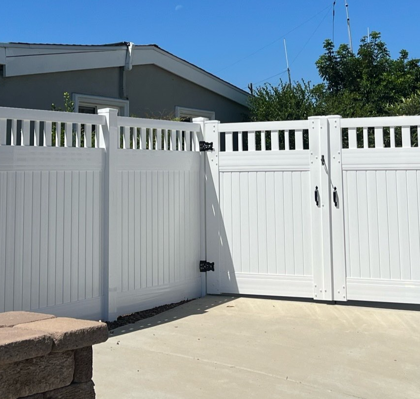 White vinyl fence and gates, open, in a sunny backyard setting.