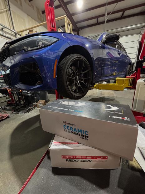 Blue sports car lifted in a garage, with CERAMIC and MOBIL 1 boxes in the foreground