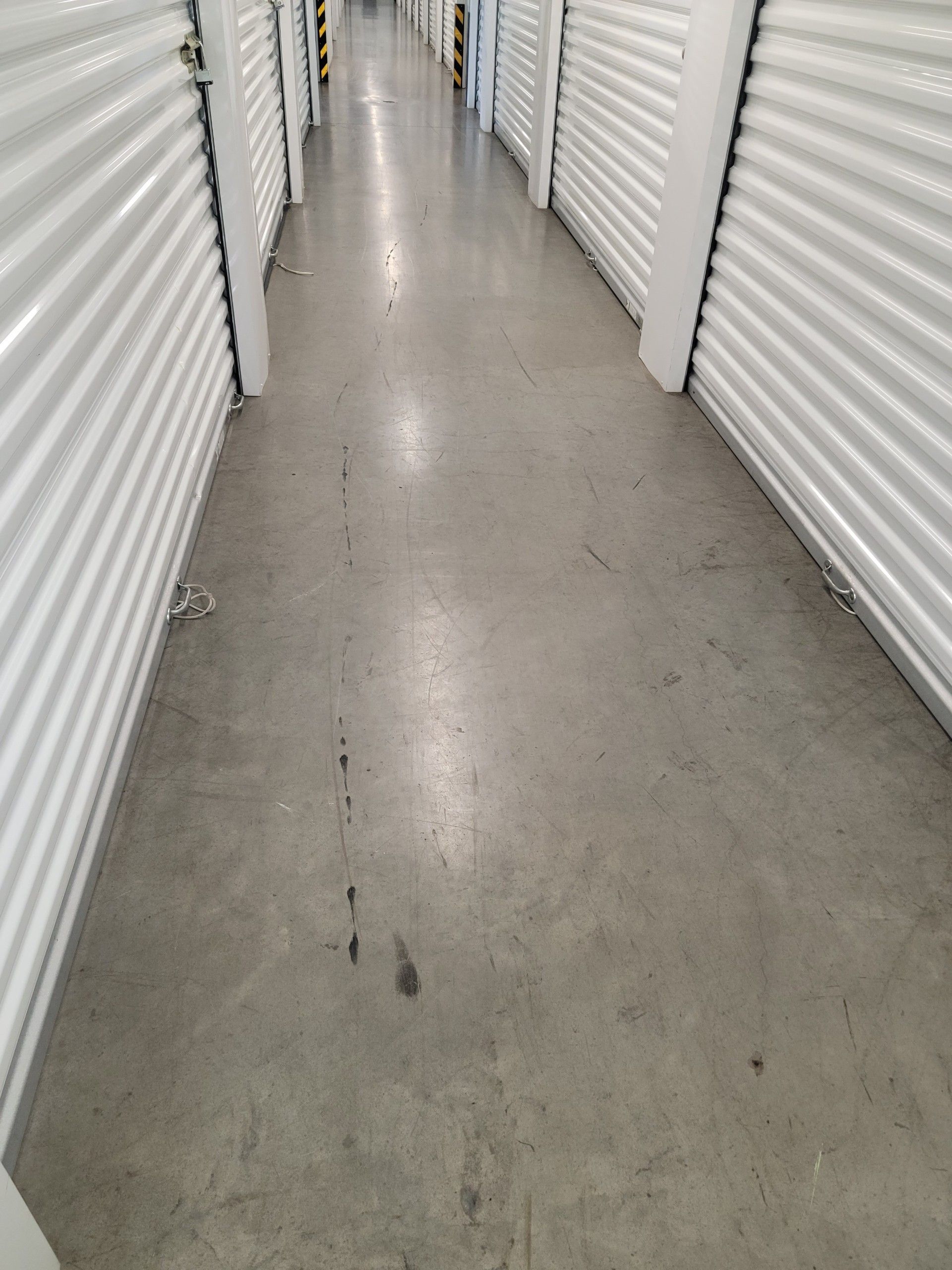 A long hallway with white shutters on the walls and a concrete floor.