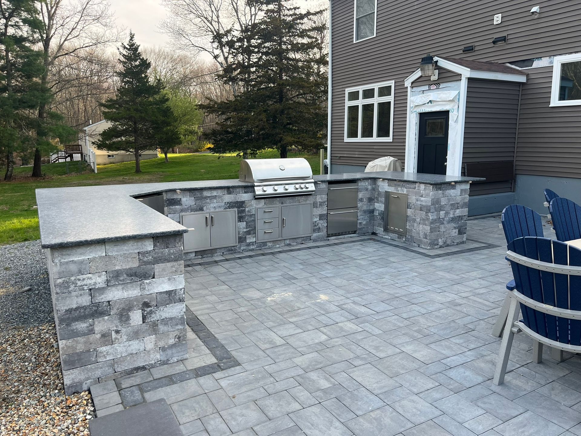 A patio with a grill and chairs in front of a house.