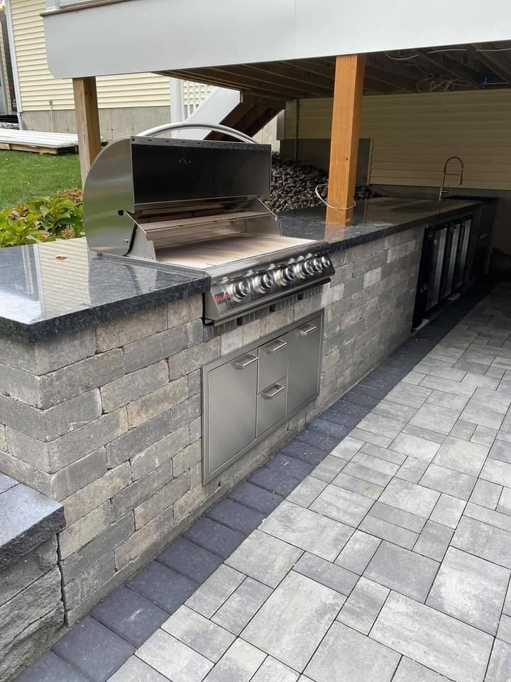 An outdoor kitchen with a grill and a sink under a canopy.