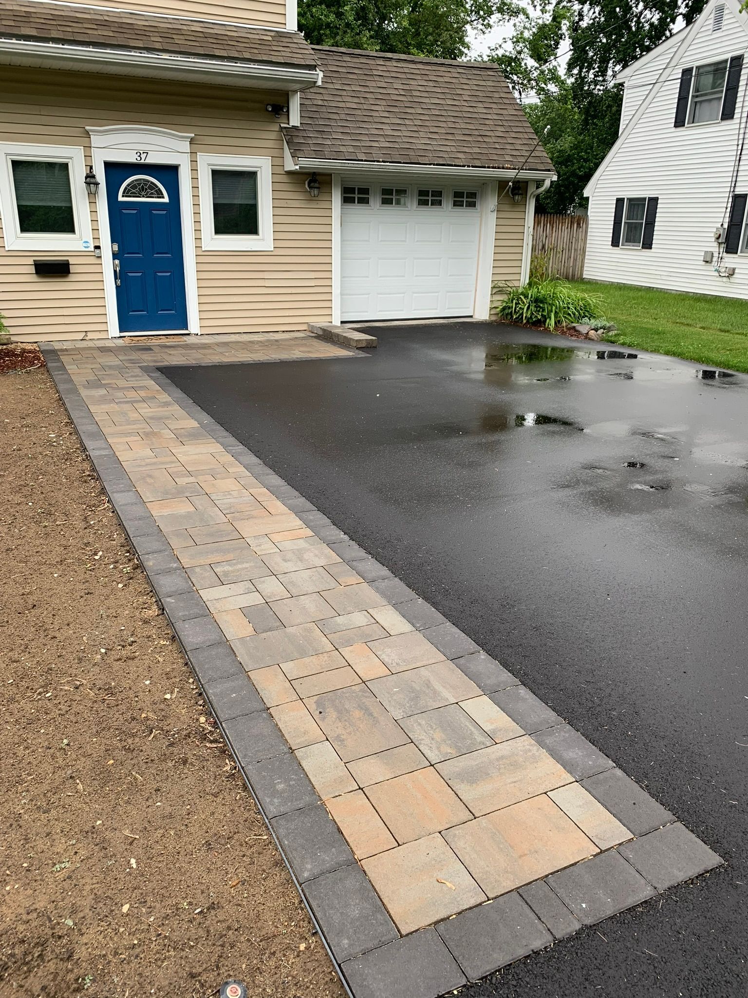 A house with a blue door and a driveway with a walkway leading to it.