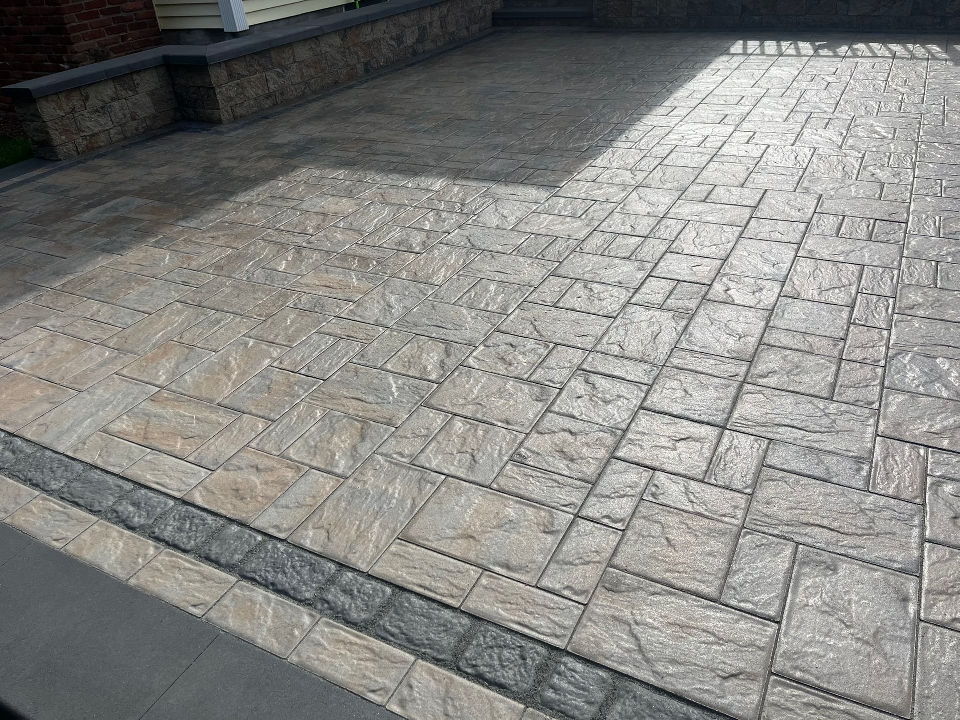 A close-up of a brick driveway with a stone wall in the background.