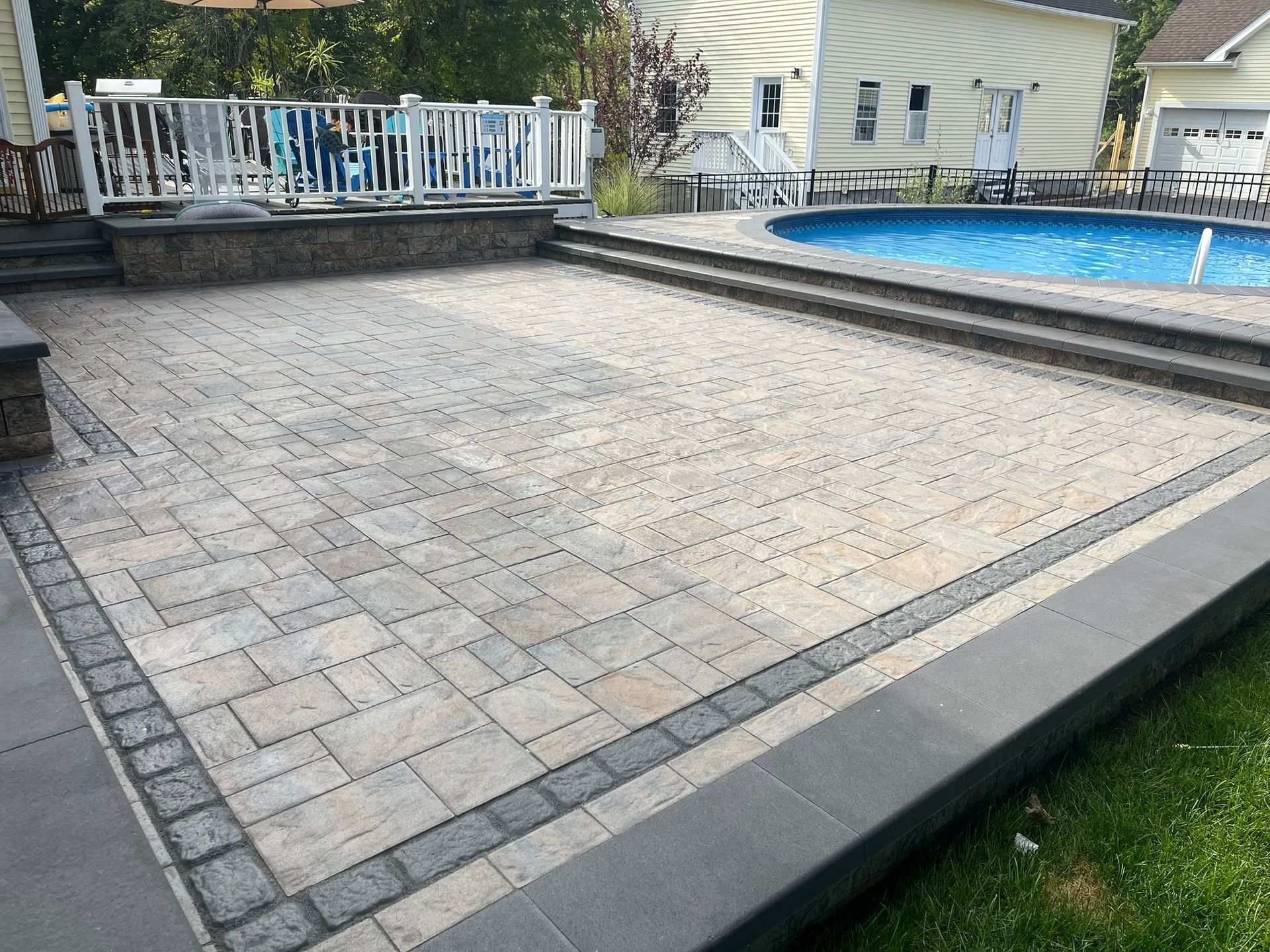 A patio with a swimming pool in the background and a house in the background.