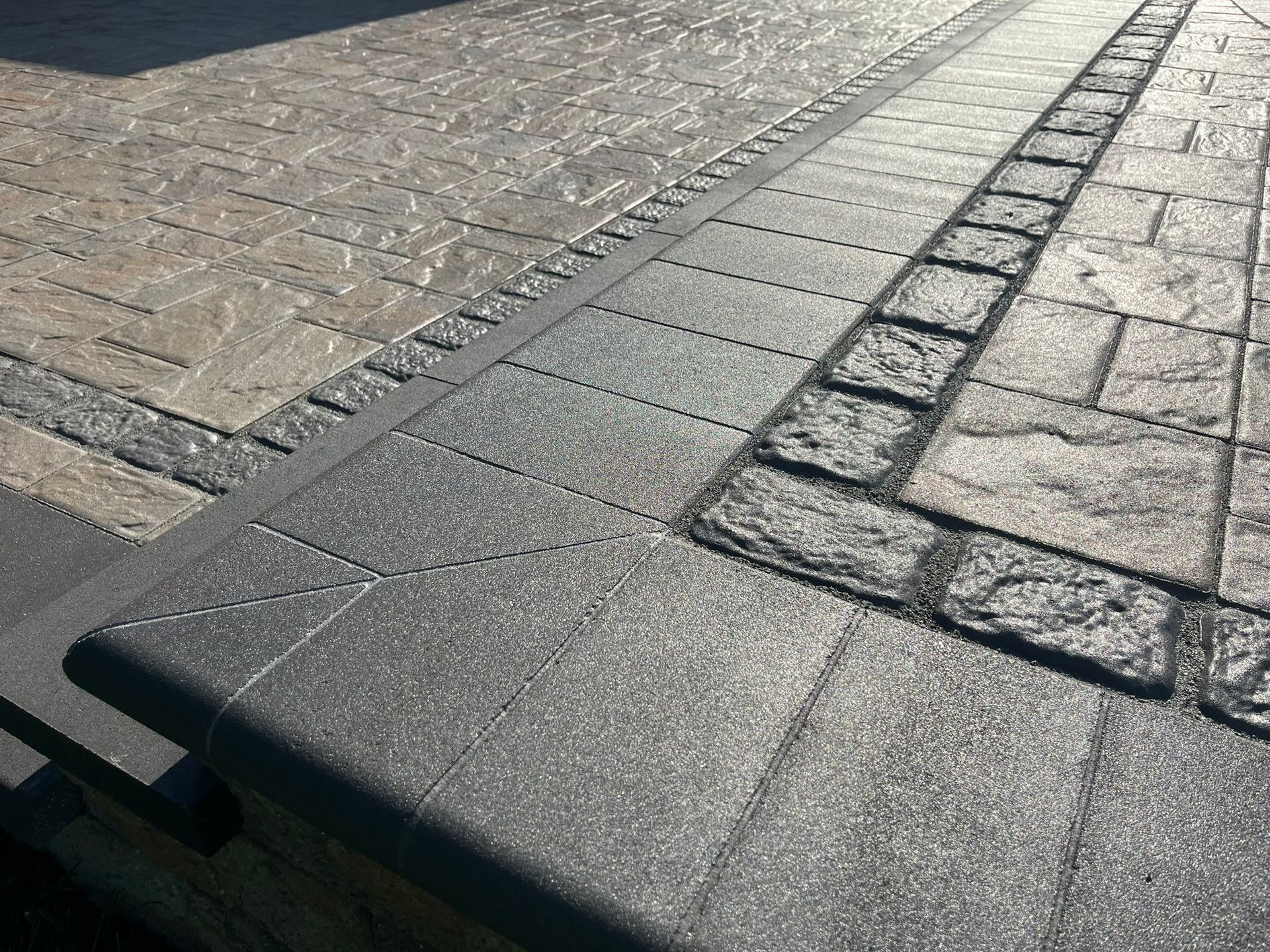 A close-up of a concrete driveway with a brick border.