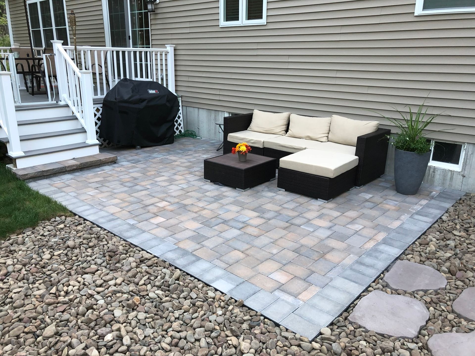 A patio with a couch, table, and grill in front of a house.