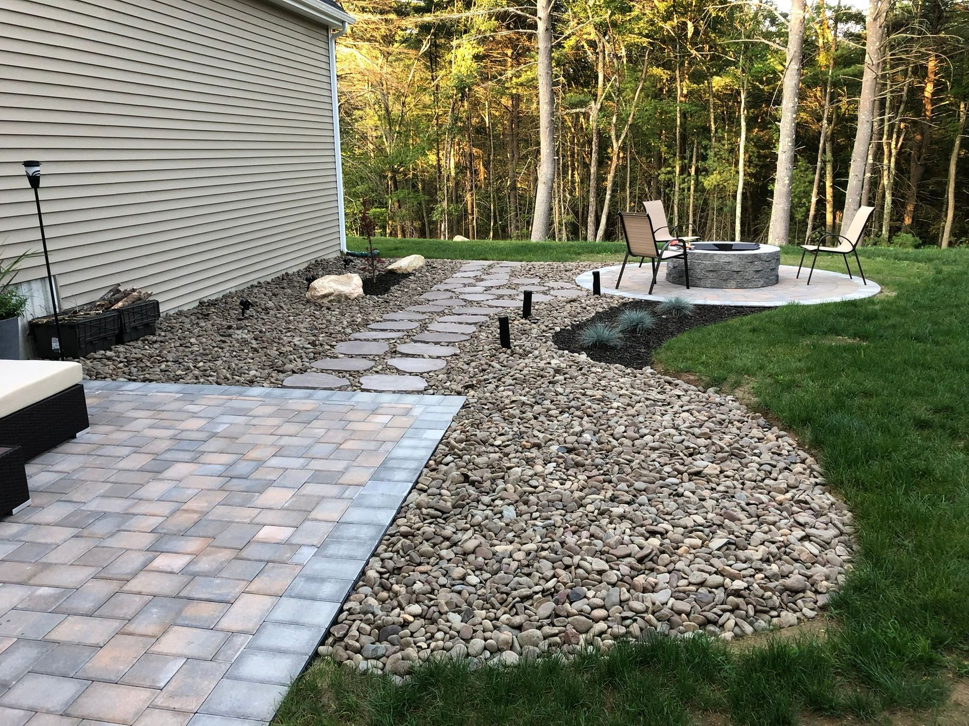 A patio with a fire pit and chairs in the backyard of a house.