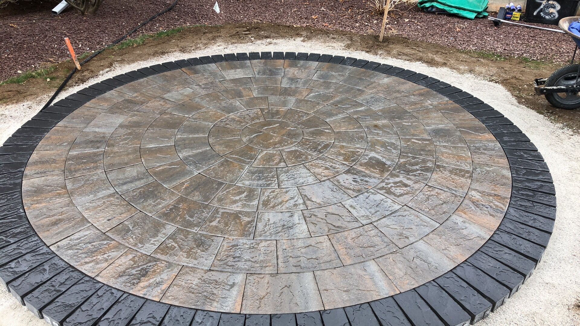 A circular patio with a black border is being built in the dirt.