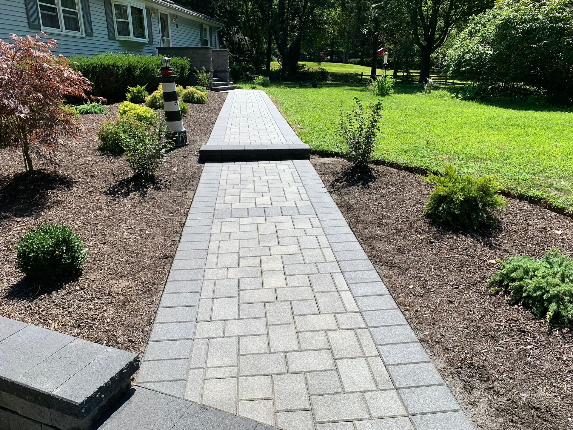 A brick walkway leading to a house with a lighthouse in the background.