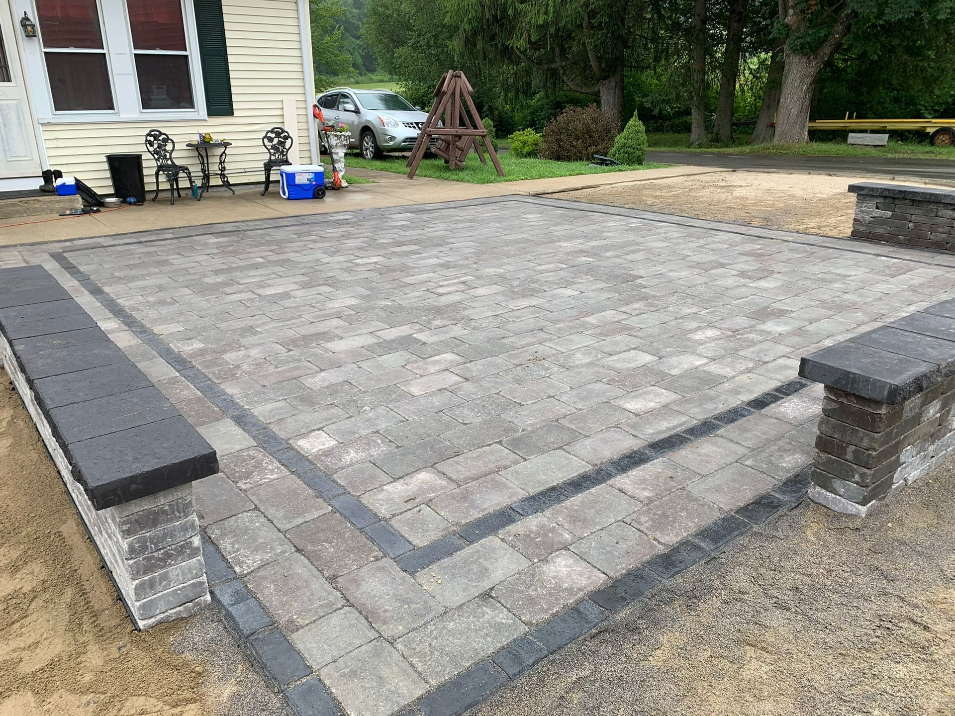 A brick patio with two benches in front of a house.