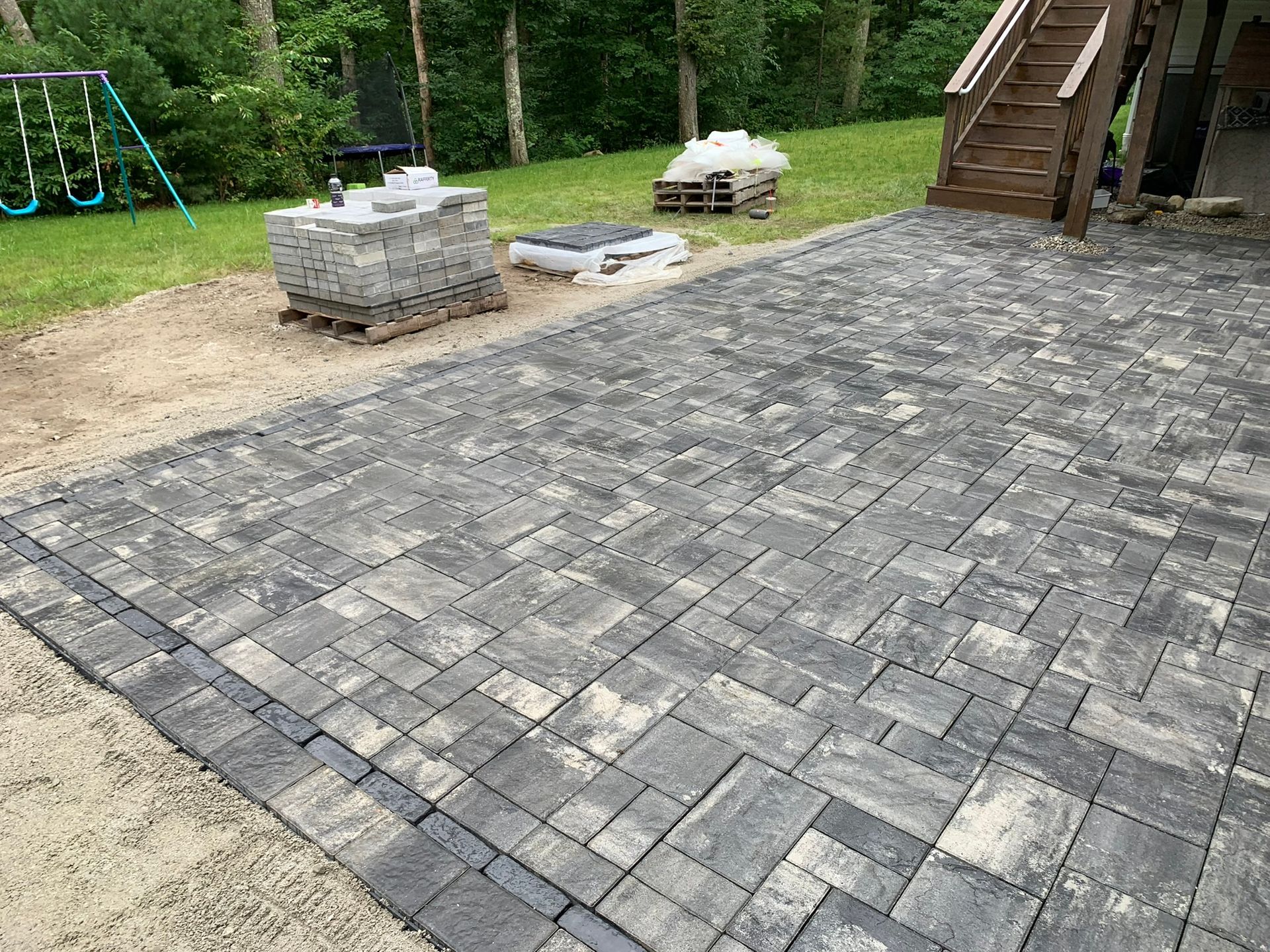 A patio is being built in a backyard with a playground in the background.