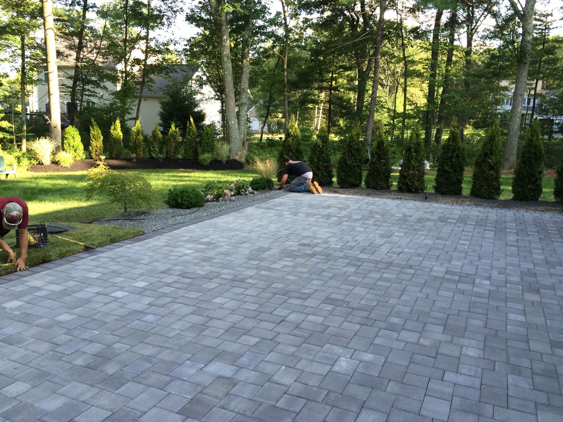 A man is working on a brick driveway in a backyard.