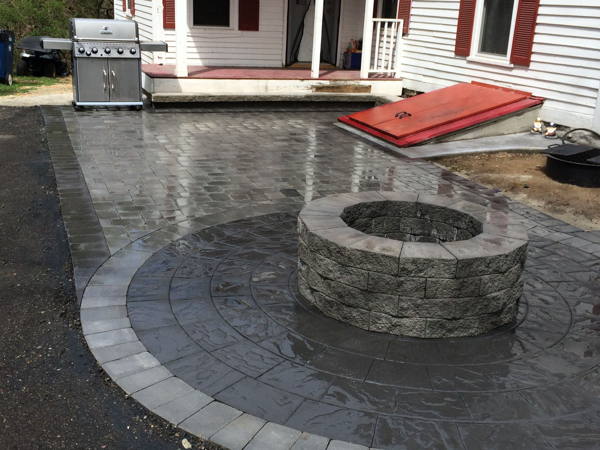 A fire pit is in the middle of a patio in front of a house.