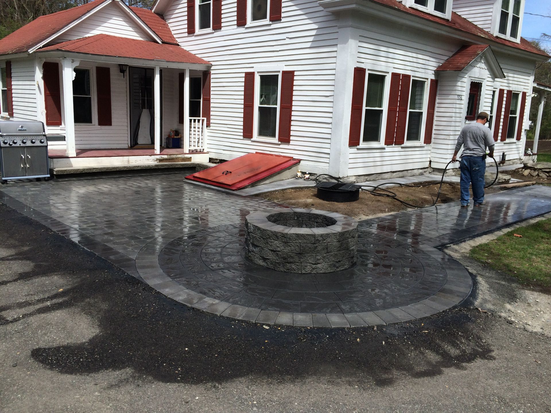 A white house with red shutters and a fire pit in front of it
