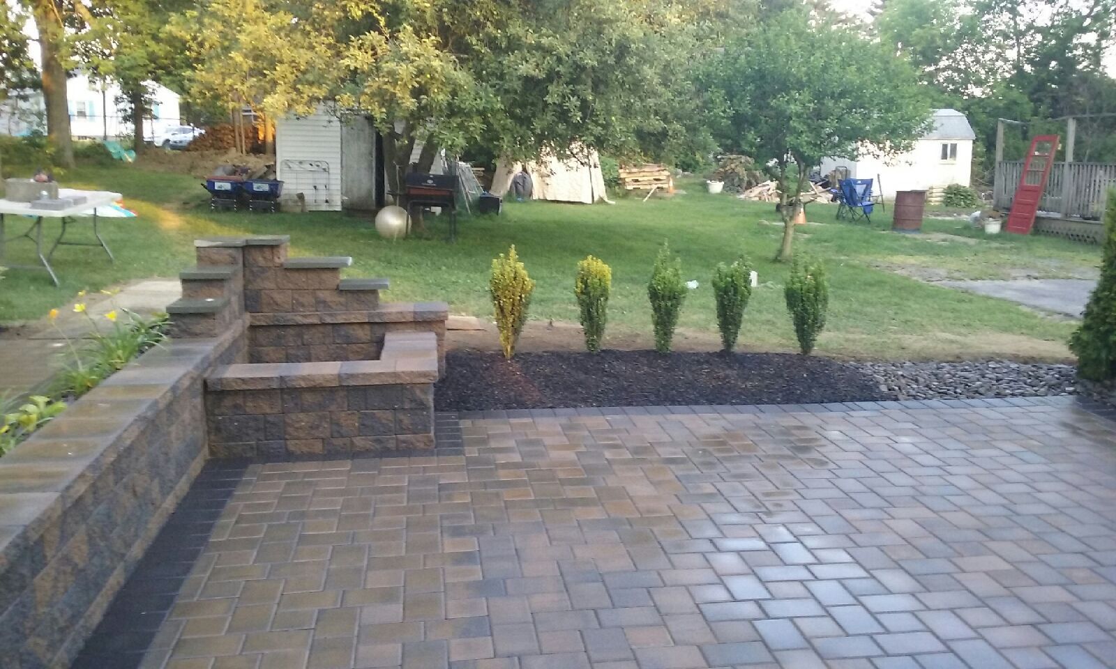 A brick patio with a wall and plants in the backyard