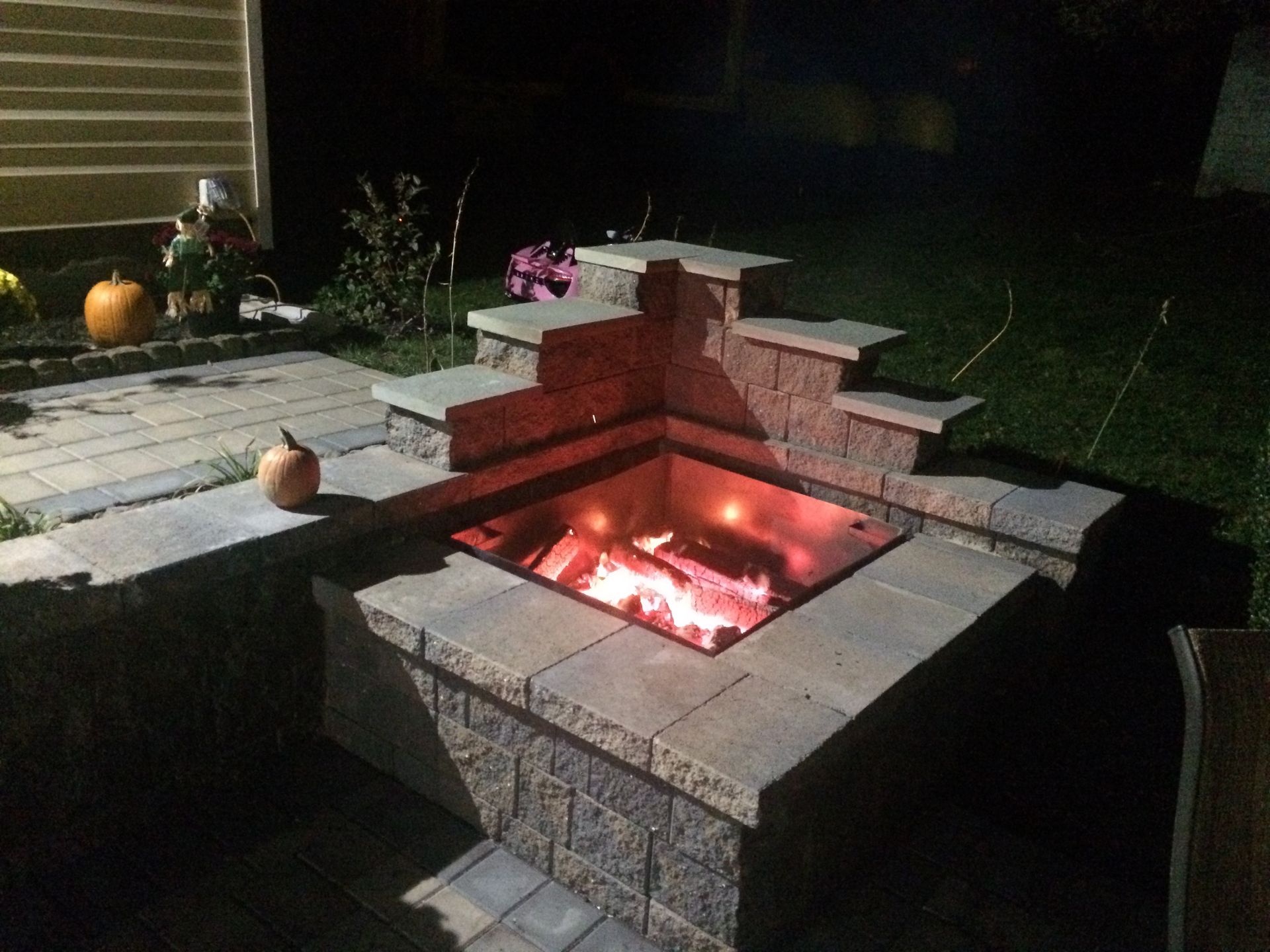 A fire pit is lit up at night in a backyard.