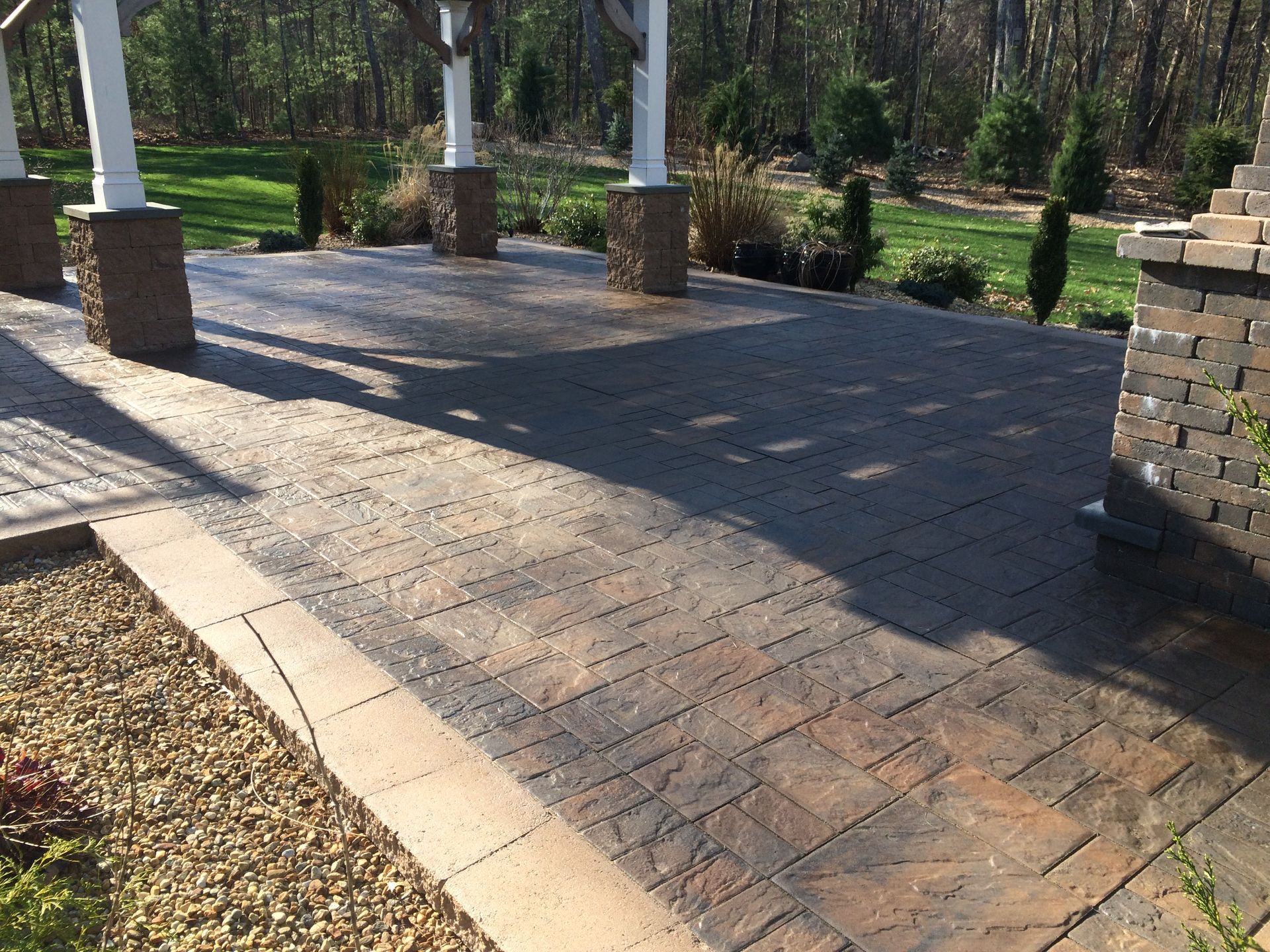 A brick walkway leading to a patio with trees in the background
