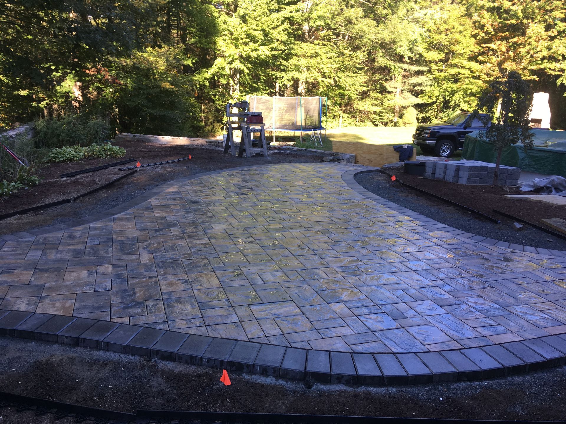 A brick patio is being built in a backyard with trees in the background