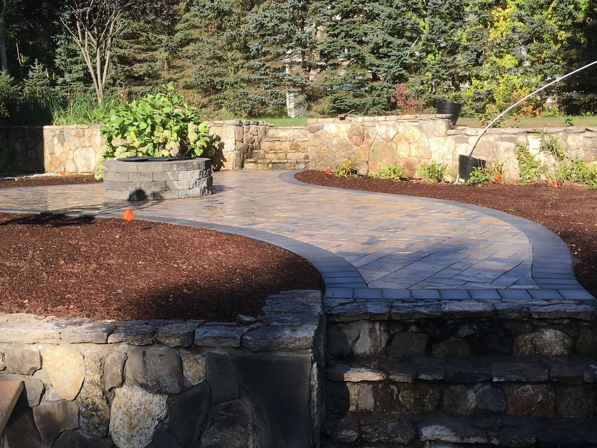 A stone walkway going through a garden with trees in the background