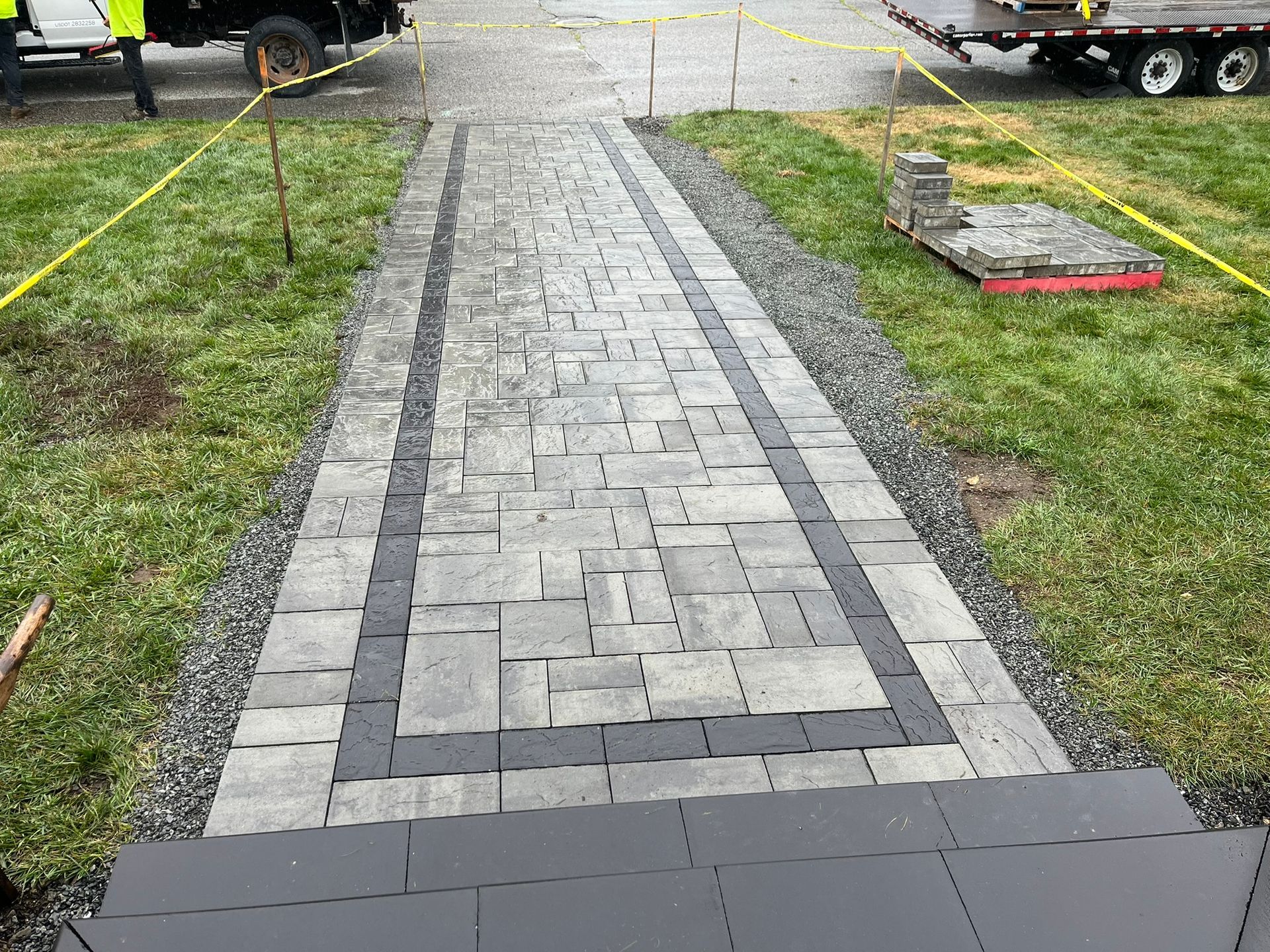 A brick walkway is being built in a grassy area next to a truck.