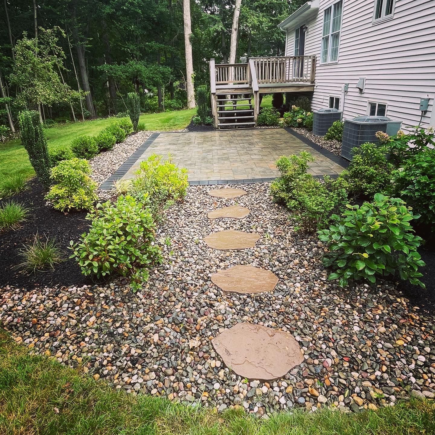 A stone walkway leading to a deck in the backyard of a house.