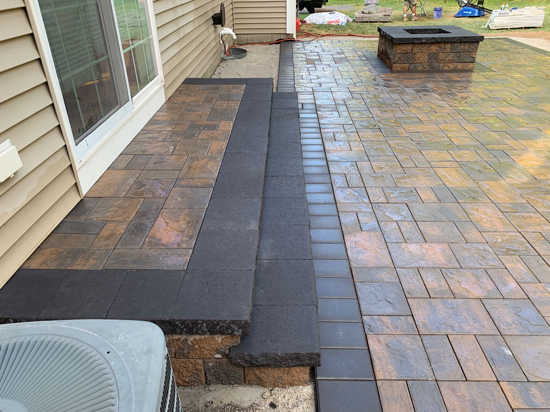 A brick patio with steps and a fire pit next to a house.