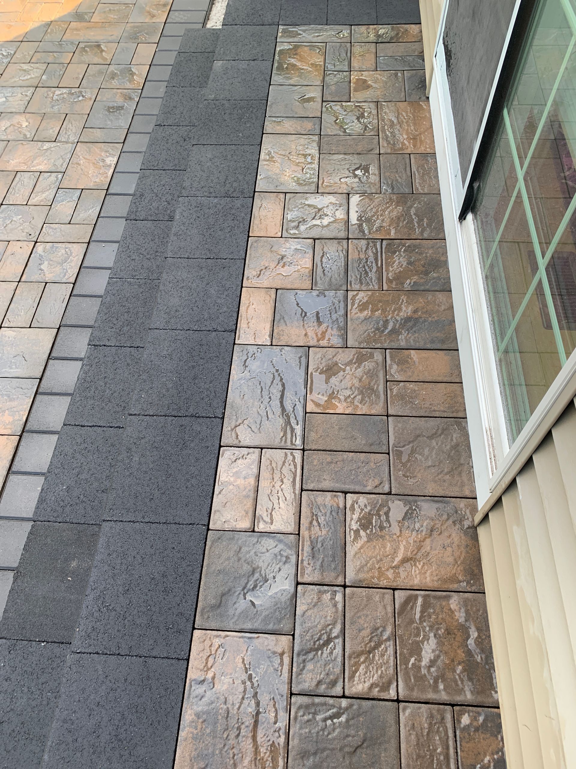 A brick walkway with a black border is next to a house.