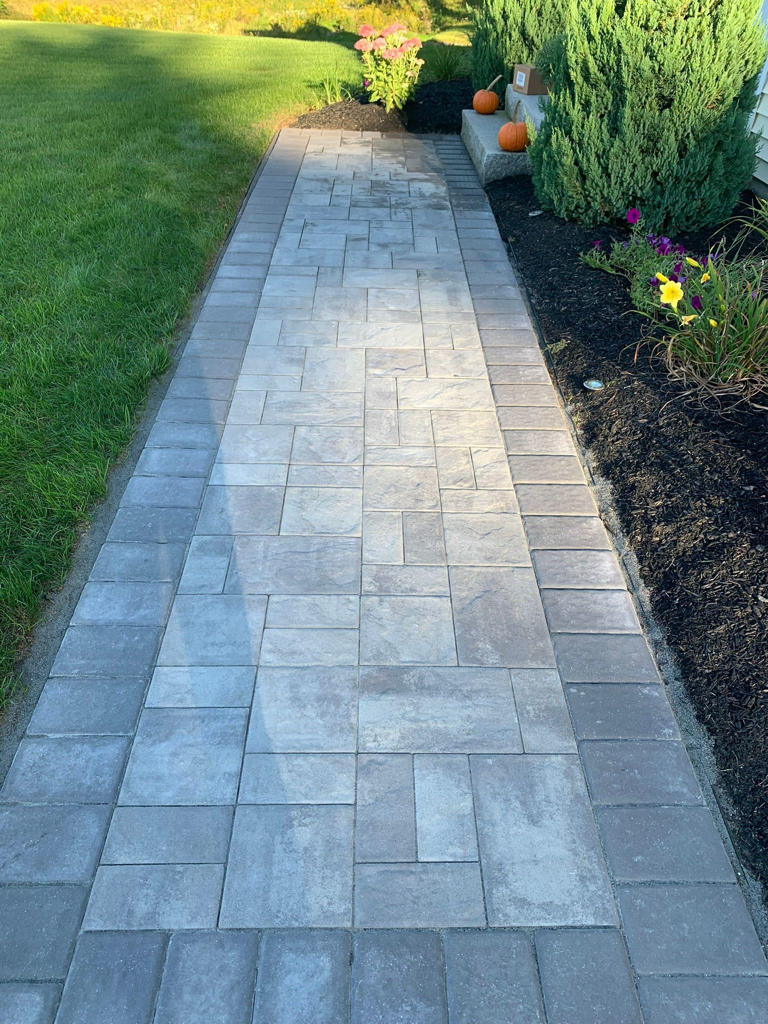 A brick walkway leading to a yard with pumpkins on the side.