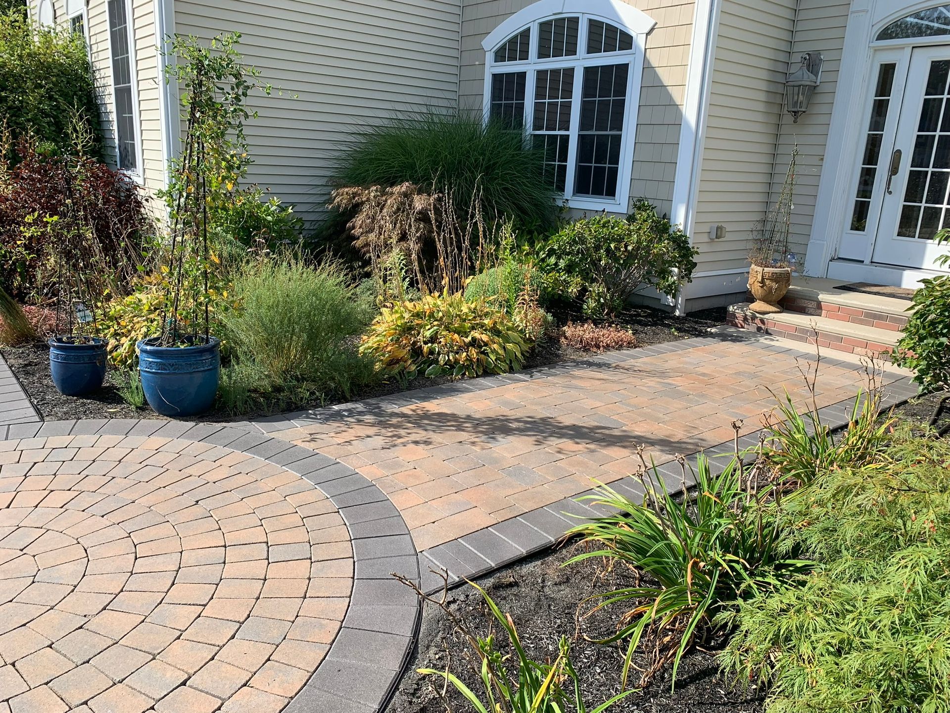 A brick walkway leading to a house with potted plants in front of it.