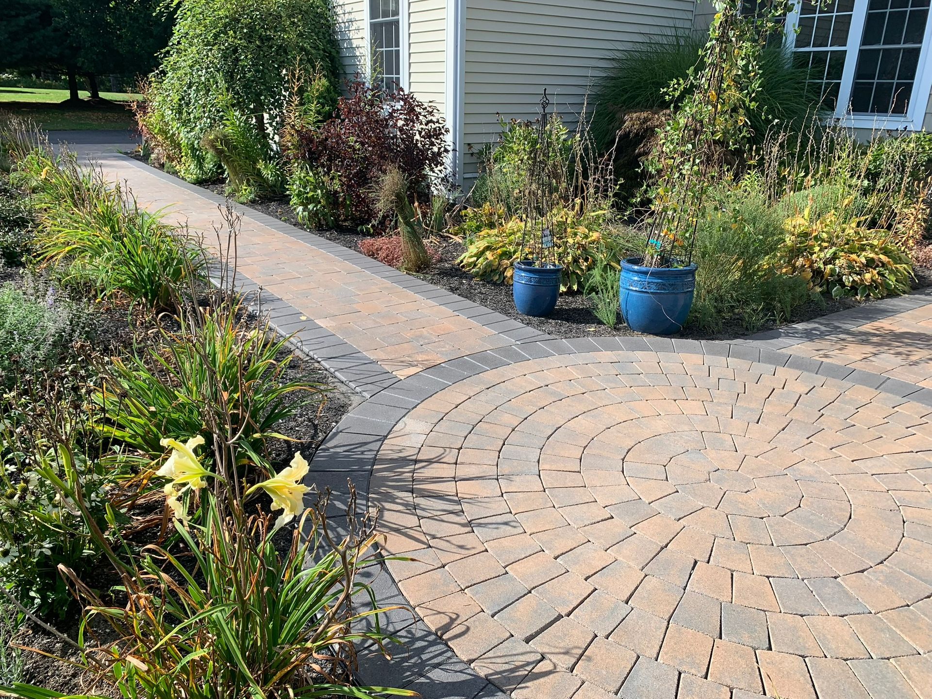 A brick walkway surrounded by potted plants and flowers in front of a house
