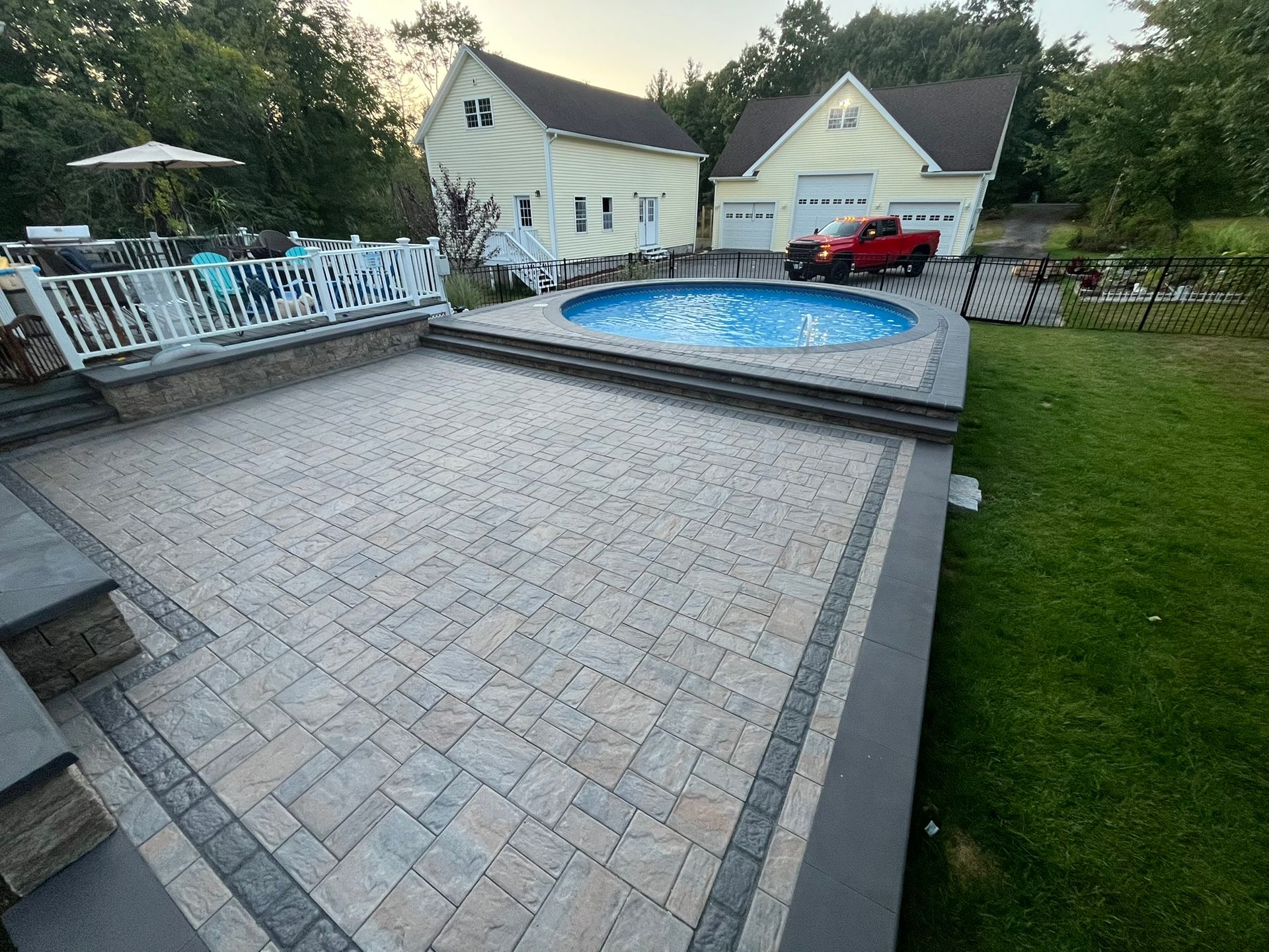 A red truck is parked in front of a large swimming pool.