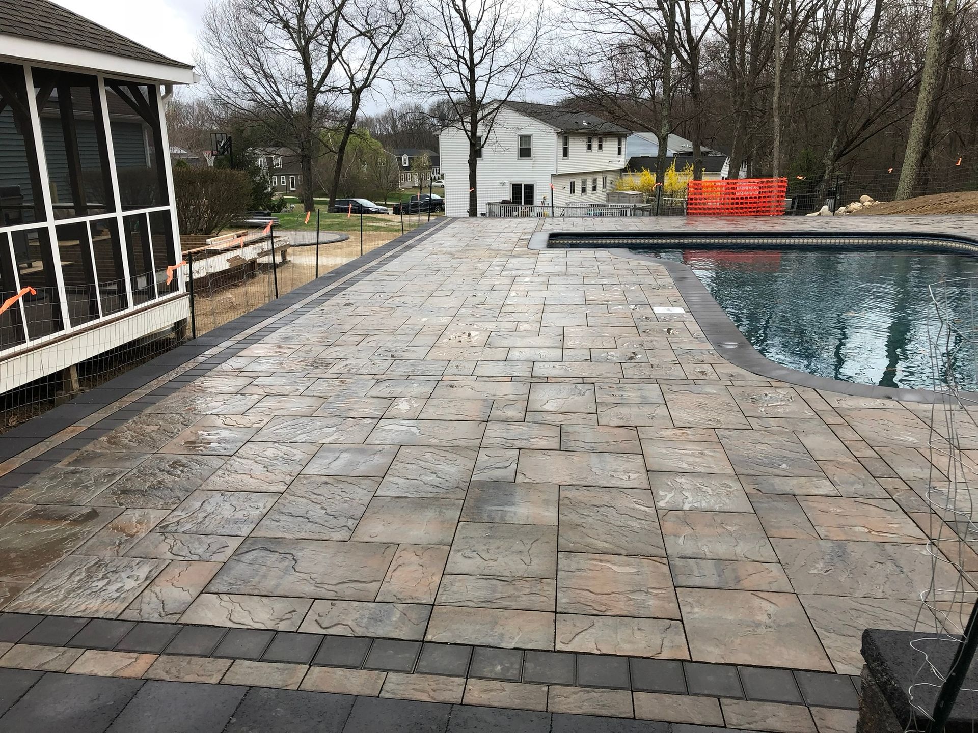 A patio with a swimming pool in the background and a screened in porch.