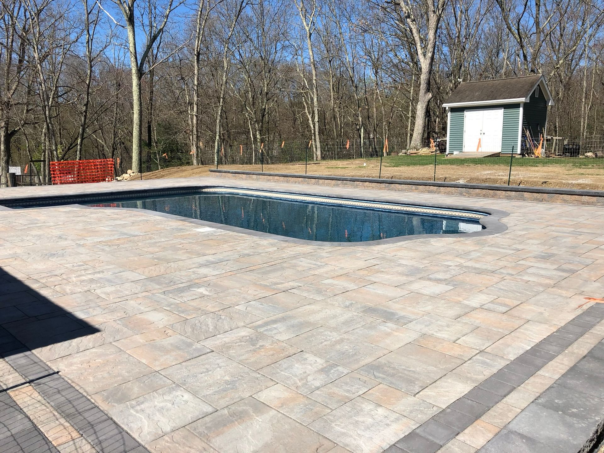 A large swimming pool is surrounded by a brick patio.