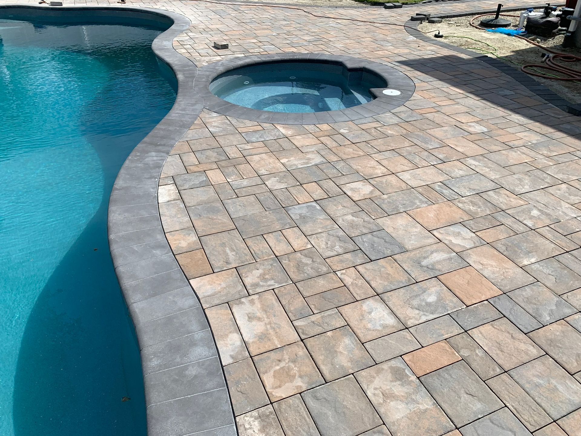 A brick patio next to a swimming pool with a hot tub in the middle.